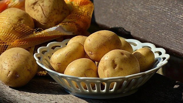 Brambory v bílé mřížové misce vedle sítě na dřevo.