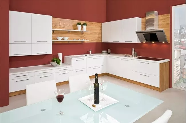 Moderní kuchyň s bílými skříněmi, červenou stěnami a jídelním stolem.