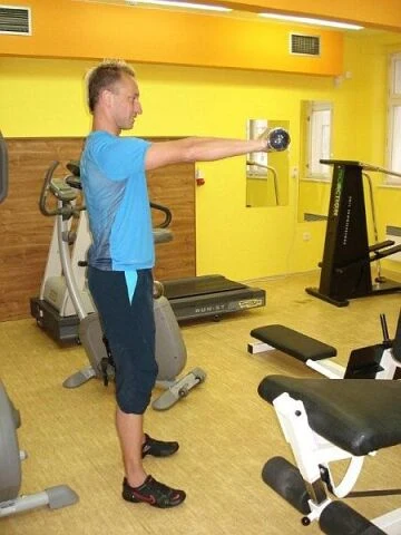 Muž cvičí ramenní svaly s váhou v posilovně.