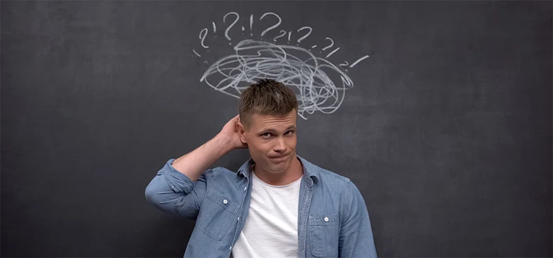 Muž se třese hlavou před tabulí s otazníky jako příznak ADHD.