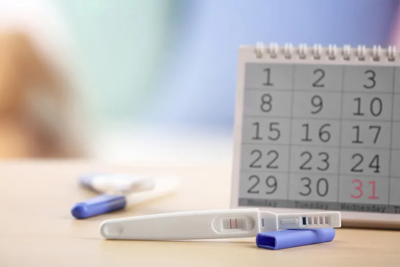 Těhotenský test s pozitivním výsledkem vedle kalendáře ukazující zpoždění menstruace.