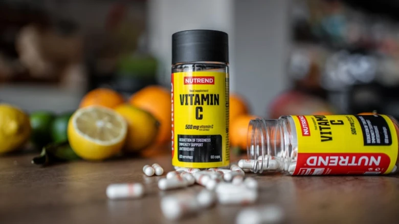 Fľaše s vitamínem C a tobolky na dřevěném stole.
