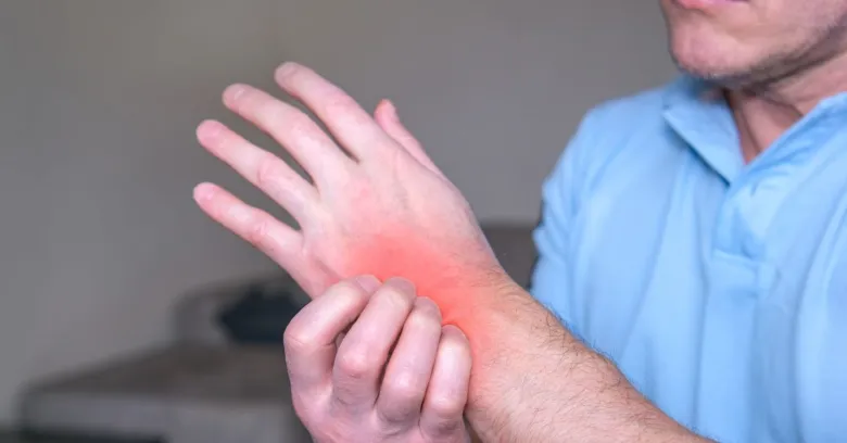 Muž drží ruku s červeným zářivým místem ukazujícím bolest.