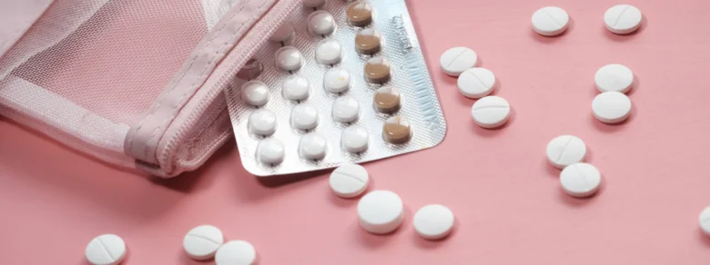 Blistry s pilulkami pro oddálení menstruace na růžovém pozadí.