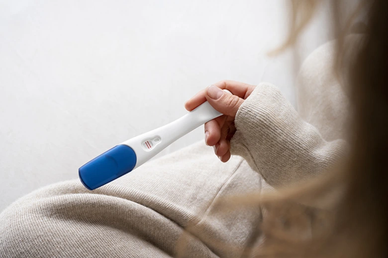 Žena drží těhotenský test s pozitivním výsledkem.