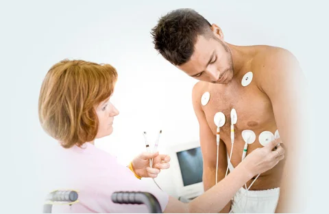 Připevňování elektrod pro EKG k hrudi pacienta lékařkou.