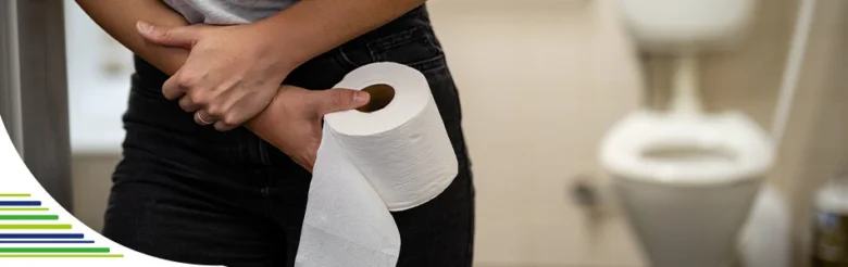Osoba drží toaletní papír v koupelně s bolestí břicha.