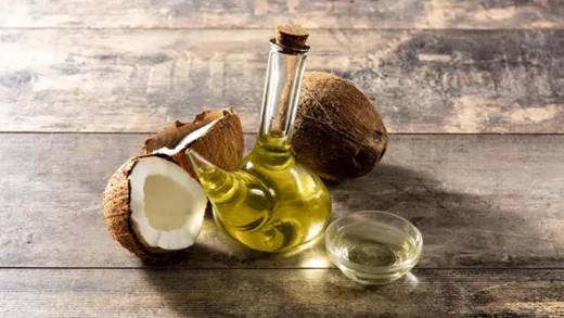 Skleněná láhev kokosového oleje s ořechy na dřevě.