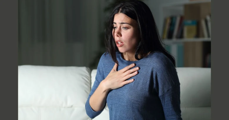 Žena sedí na gauči s rukou na hrudi při hyperventilaci.