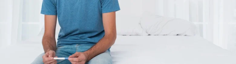 Muž sedící na posteli s těstovinou pro domácí test.