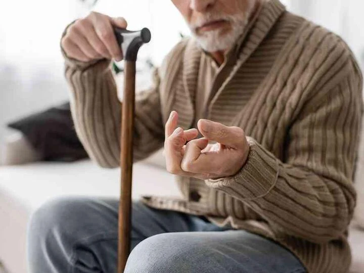 Starší muž s holí ukazuje na třes ruky při parkinsonismu.