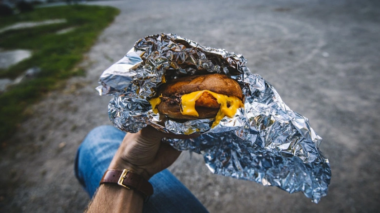 Ruka drží burger zabalený v hliníkové fólii venku.