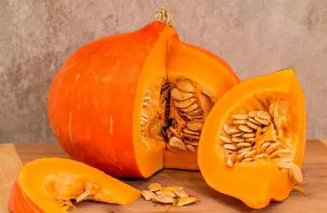 Nakrájená oranžová dýně s viditelnými semínky na dřevě.