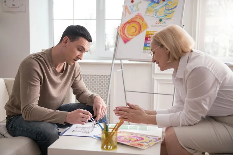 Muž kreslí pod vedením terapeuta při arteterapii.
