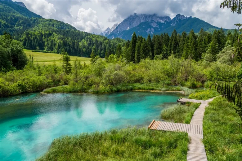 Modré jezero v zeleném krajině s horami na pozadí.