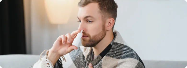 Muž používá nosní sprej pro léčbu nachlazení.