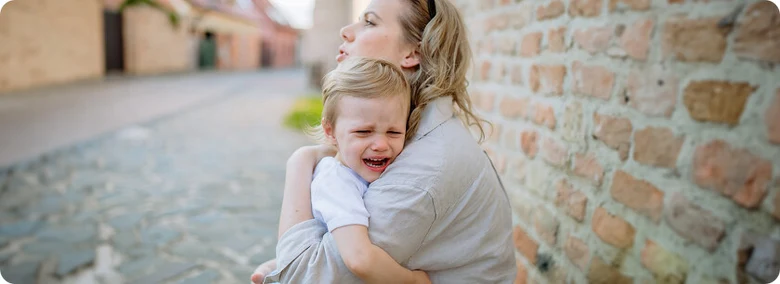 Žena objímá pláčícího dítěte u staré cihlové zdi.