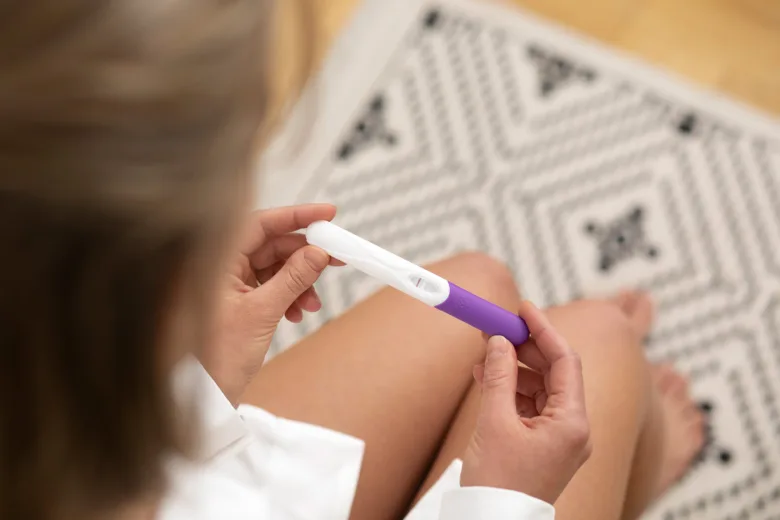 Žena drží v rukou těhotenský test s pozitivním výsledkem.