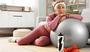 Žena v sportovním oblečení sedí na podlaze s fitballem.