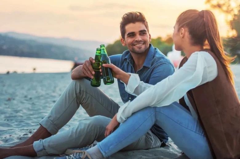 Muž a žena pijí pivo na pláži při západu slunce.