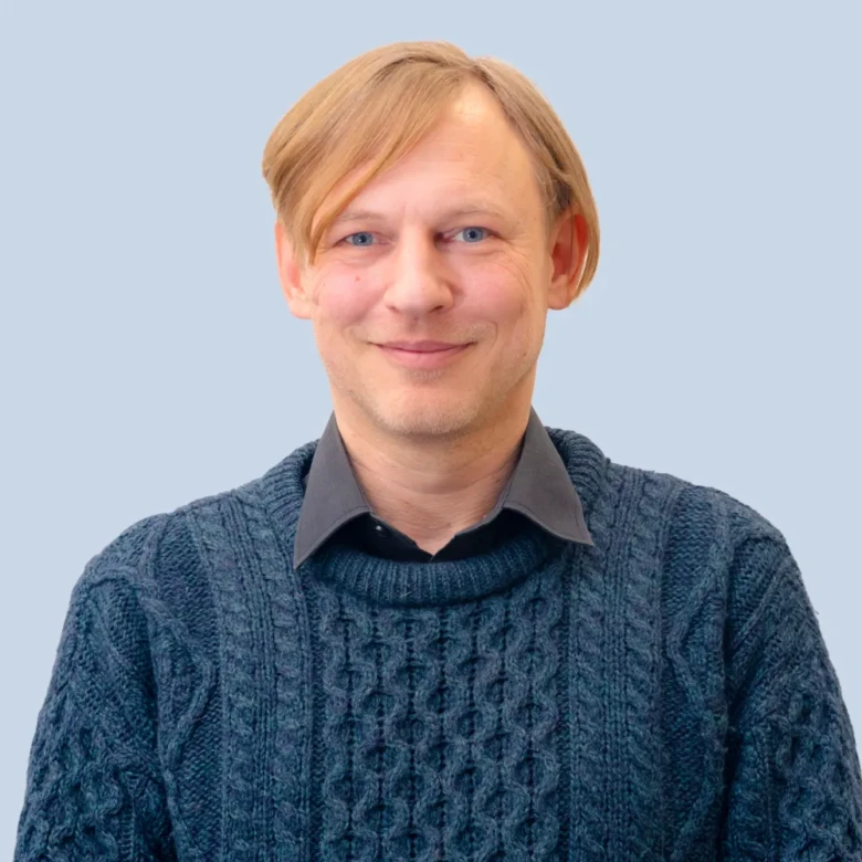 Muž v modrém svetrku na světlemodrém pozadí.