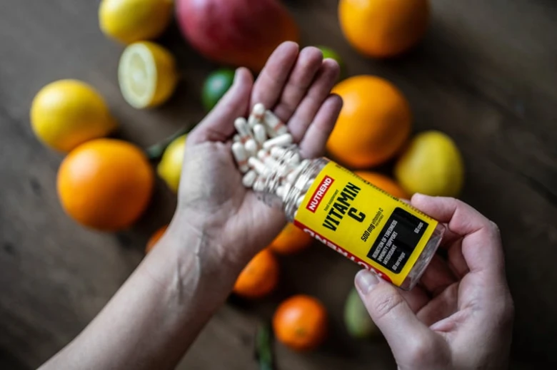Ruce s tabletami vitamínu C mezi citrusovými plody.