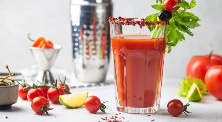 Sklenička s krvavou Marií obklopená čerstvými ingrediencemi jako rajčata.