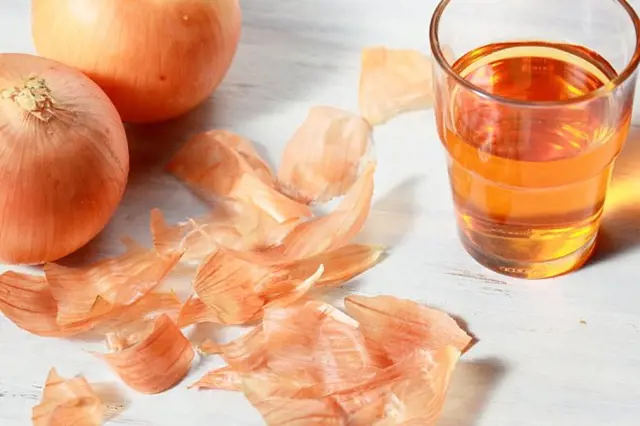 Cibule s loupanými slupkami a sklenicí cibulové vody na dřevěném povrchu.