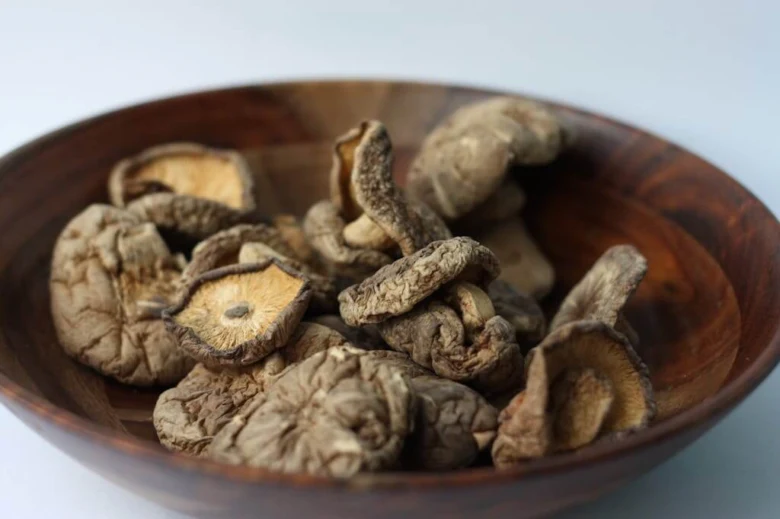 Sušené houby shiitake v dřevěné míse na bílém pozadí.