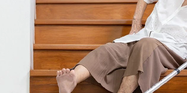 Starší osoba sedí na schodech s holinkou kvůli osteoporóze.