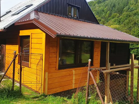 Přestavěná dřevěná chalupa s žlutými stěnami a kovovou střechou.