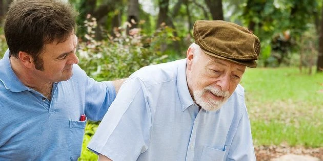 Mladý muž pomáhá starému muži s Parkinsonovou chorobou venku.