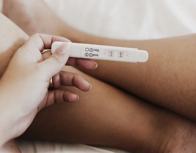Ruka drží pozitivní těhotenský test s dvěma čarami.