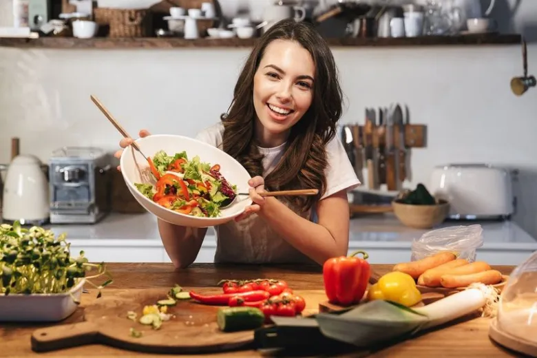 Žena drží misku čerstvého salátu s zeleninou v kuchyni.