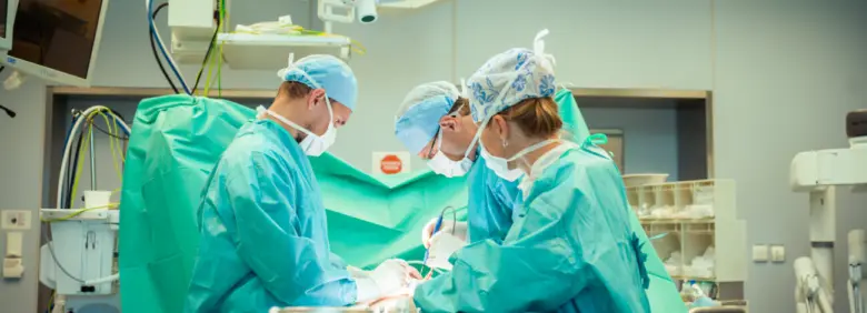 Tři lékaři operují pacienta v operační sále.