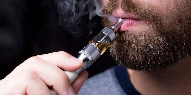 Muž kouří z elektronické cigarety s viditelným párou.