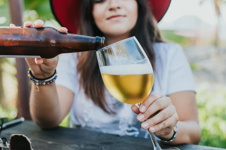 Žena nalévá pivo do sklenice venku u stolu.