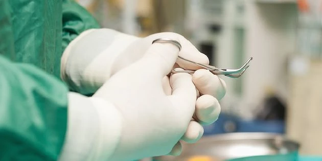 Ruce v rukavicích drží chirurgický nástroj na operačním sále.