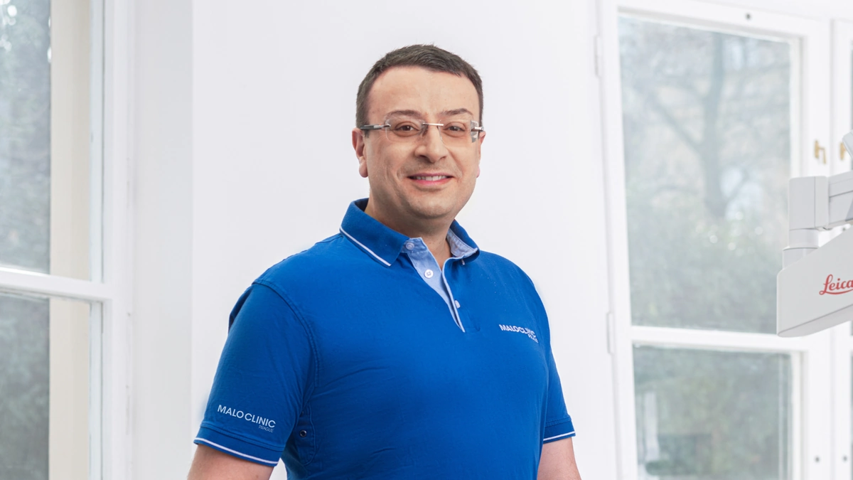 Muž v modrém tričku stojí u okna ve stomatologické ordinaci.