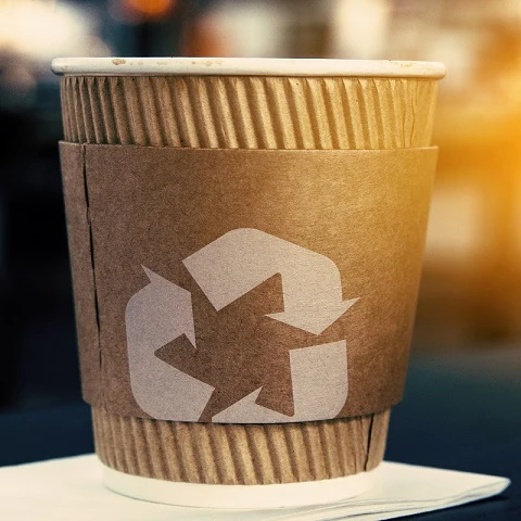 Kávová šálka z papíru s logem pro recyklaci na rukávu.
