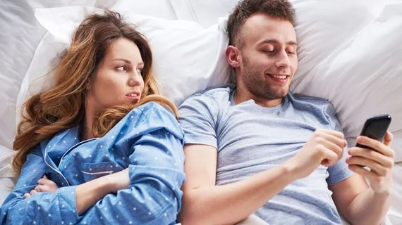 Muž a žena v posteli s mobilním telefonem