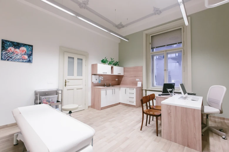 Moderní lékařský pokoj s vyšetřovacím stolem a pracovištěm pro lékaře.