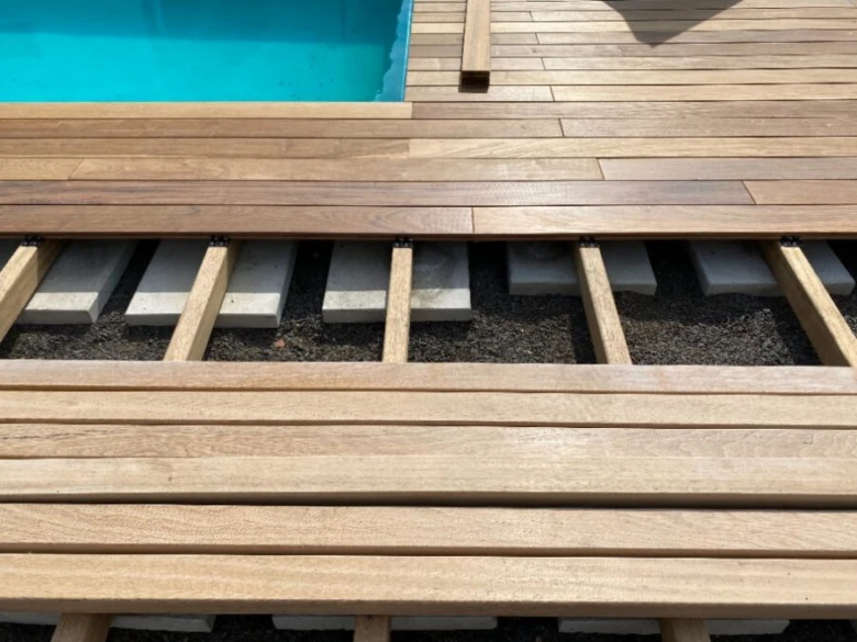 Detail dřevěné terasy s prkny, trámy a betonovými bloky u bazénu.
