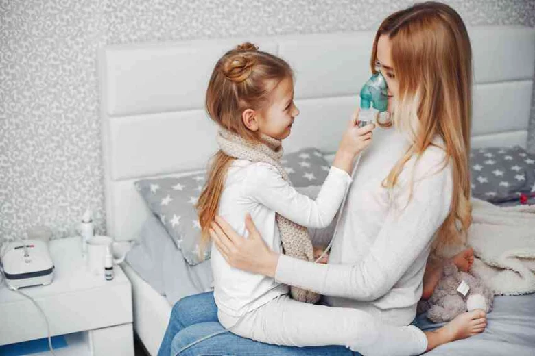 Matka pomáhá dceři používat inhalátor s maskou doma.