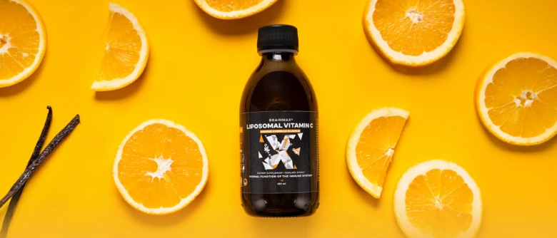 Fialová lahvička s vitamínem C mezi čerstvými pomeranči na žlutém pozadí.