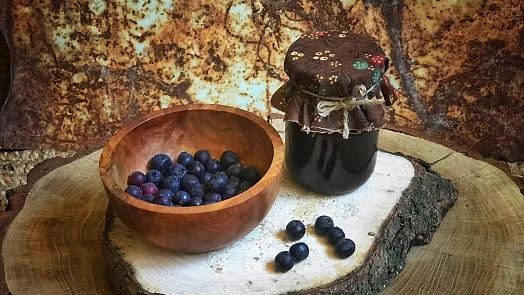 Miska s borůvkami a sklenice domácí marmelády na kousku dřeva.