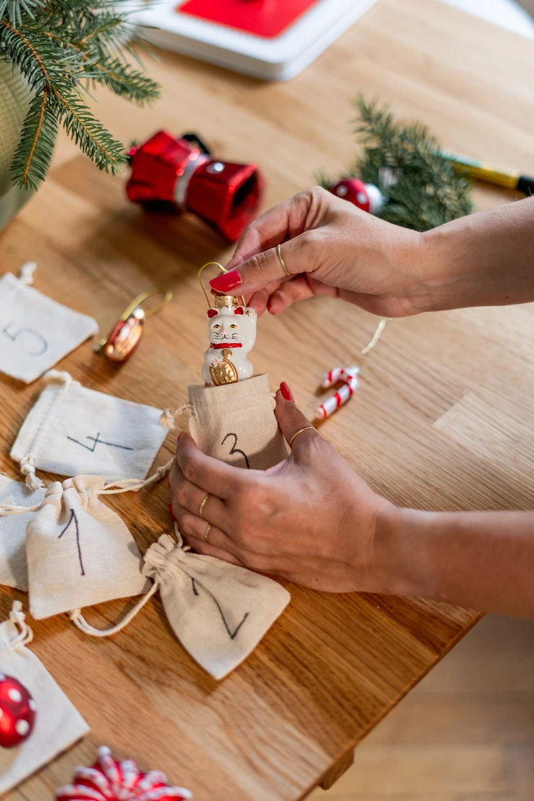 Ruce vkládají ozdobu do sáčku pro adventní kalendář na stůl.