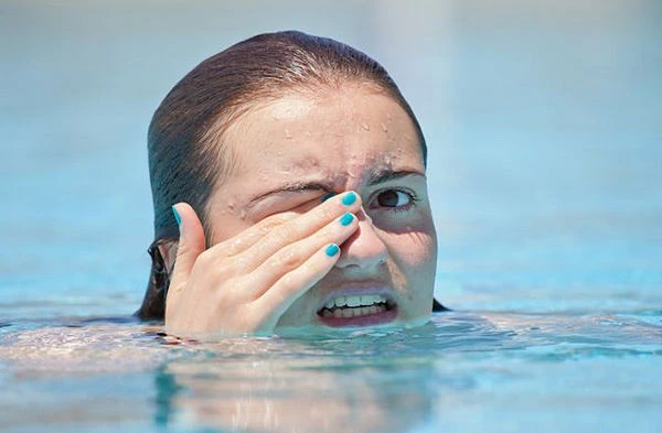 Žena v bazénu drží ruku k obličeji kvůli podráždění od chloru.