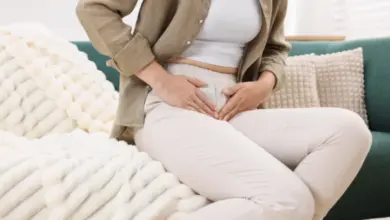 Žena sedící na gauči s rukama na břiše v bolesti.