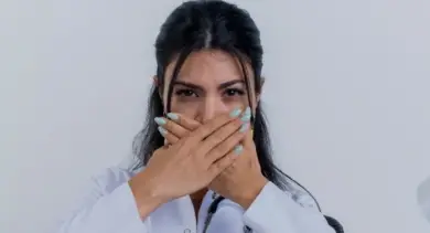 Žena v bílé košili zakrývá nos rukama.